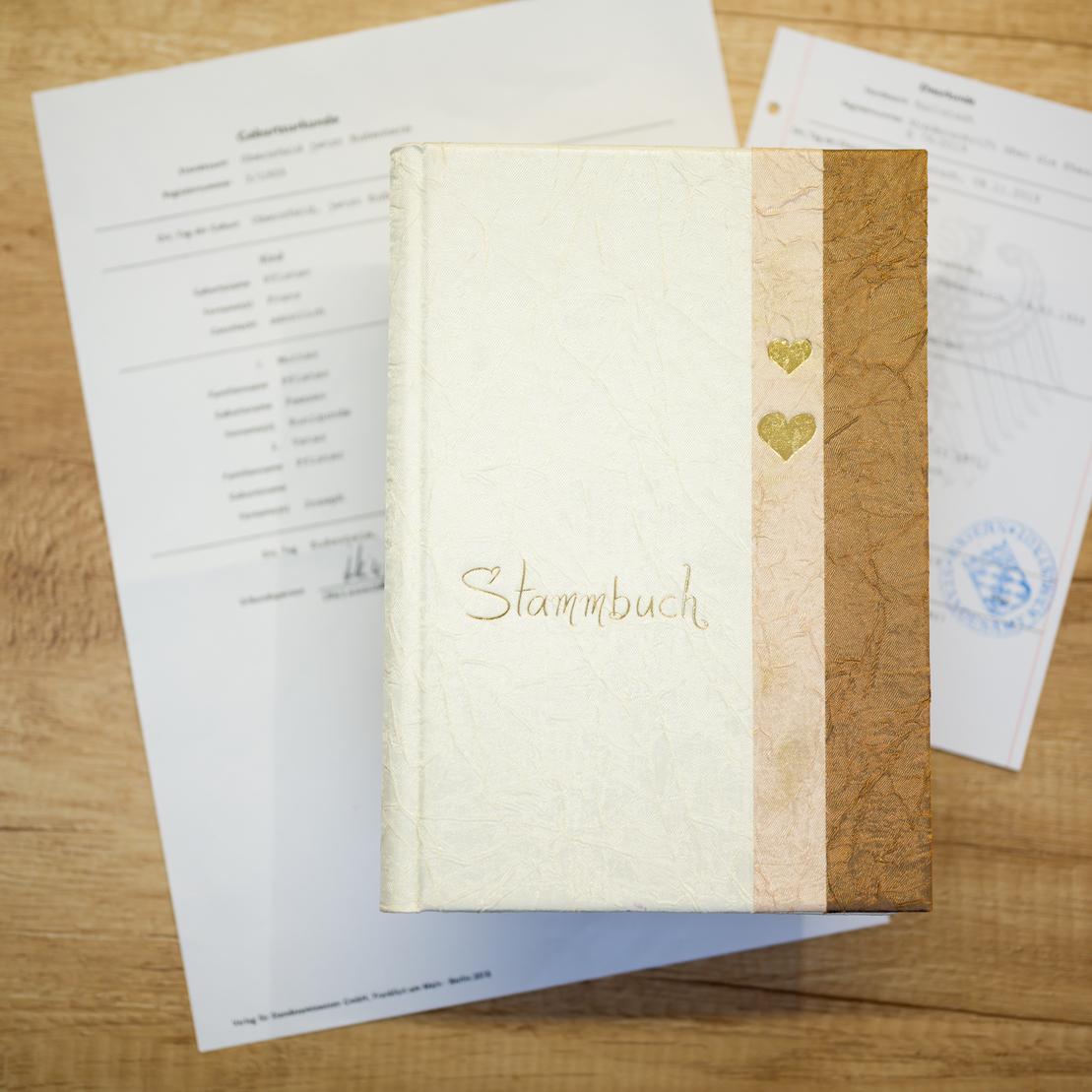 Stammbuch mit goldener Schrift und Herzen, daneben zwei amtliche Dokumente auf einem Holzuntergrund.