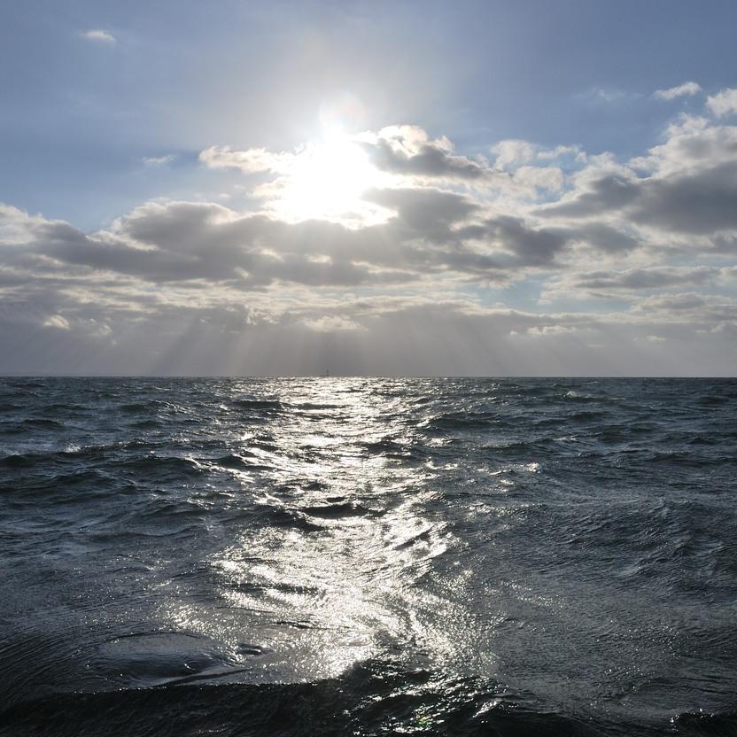 Helle Sonne über dem glanzvollen, welligen Wasser unter einem bewölkten Himmel.