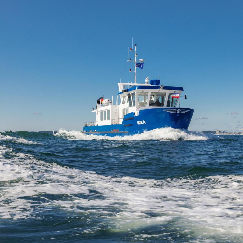 Blaues Ausflugsboot mit der Aufschrift "MIRA" fährt über wellige, schäumende Wasseroberfläche bei klarem Himmel.