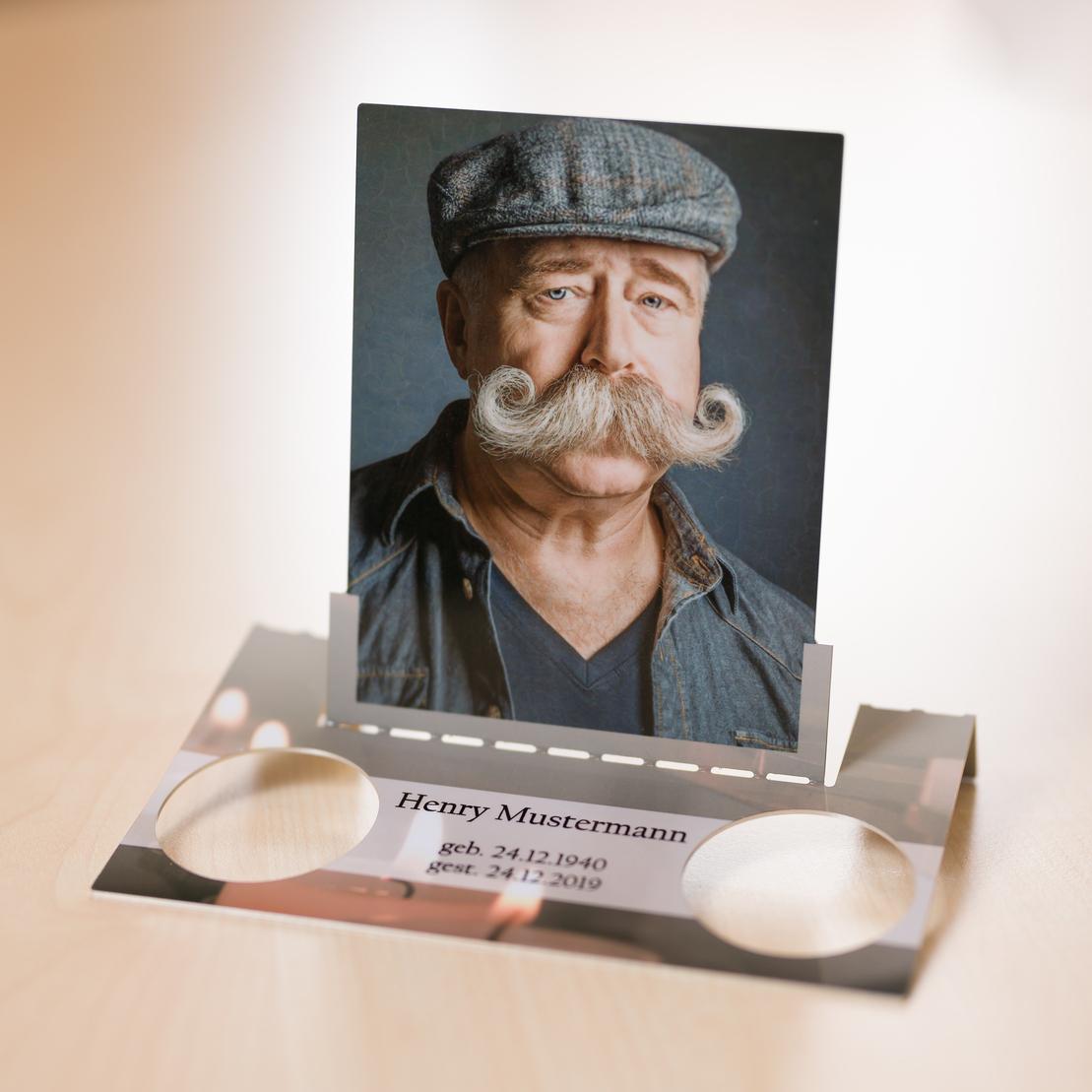 Portrait eines Mannes mit Schnurrbart und M&uuml;tze in einem Bilderhalter, mit Inschrift &uuml;ber Geburts- und Sterbedaten.