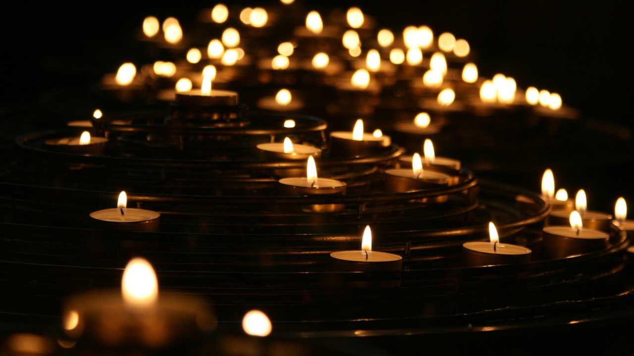 Nahaufnahme von vielen brennenden Teelichtern auf spiralförmigen Halterungen im dunklen Raum.