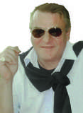 Mann mit Sonnenbrille und schwarzem Pullover um den Hals, lächelt und hält eine Zigarette in der Hand.