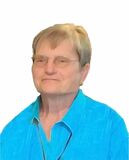 Porträt einer älteren Frau mit Brille, die ein hellblaues Hemd trägt, vor einem hellen Hintergrund.