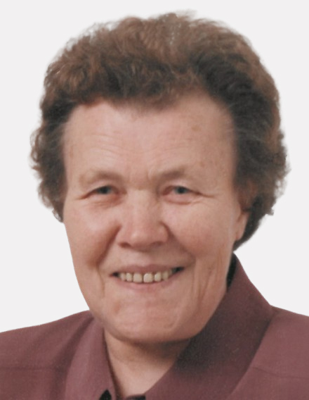 Portr&auml;t einer &auml;lteren Frau mit lockigem Haar, die in die Kamera l&auml;chelt und ein burgunderfarbenes Hemd tr&auml;gt.