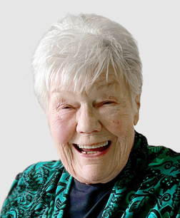 L&auml;chelnde &auml;ltere Frau mit kurzen grauen Haaren, tr&auml;gt einen gr&uuml;nen, gemusterten Schal vor einem hellen Hintergrund.