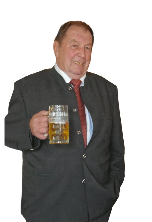 Mann in traditioneller Kleidung h&auml;lt ein gro&szlig;es Glas Bier, l&auml;chelnd und stehend mit einer Hand in der Hosentasche.