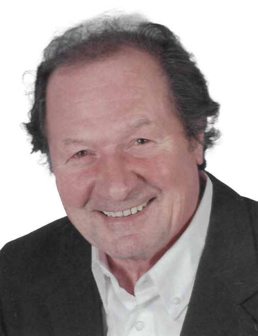 Portrait eines l&auml;chelnden Mannes mit mittellangen, dunklen Haaren, in einem schwarzen Jackett und wei&szlig;em Hemd.