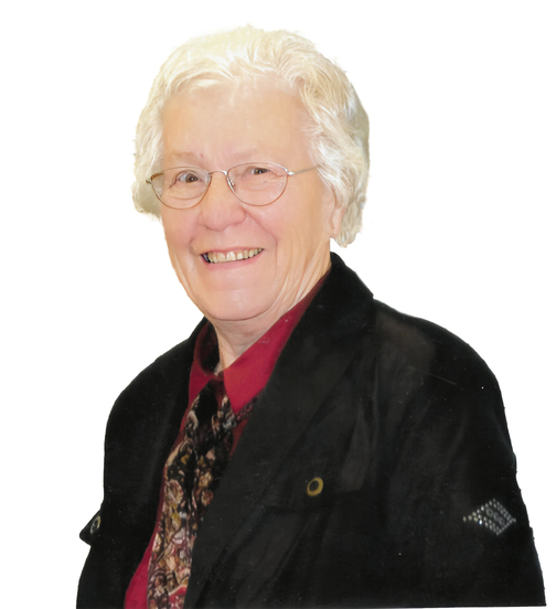 L&auml;chelnde &auml;ltere Frau mit Brille, blonden Locken, schwarzer Jacke und gemusterter Krawatte auf wei&szlig;em Hintergrund.