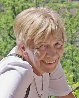 L&auml;chelnde &auml;ltere Frau mit kurzem, blondem Haar, vor gr&uuml;nem Hintergrund im Freien.