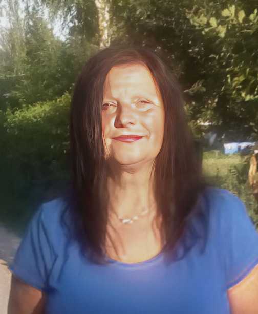Portr&auml;t einer Frau mit langen, dunklen Haaren und blauem Shirt, vor einer gr&uuml;nen, bewaldeten Kulisse.