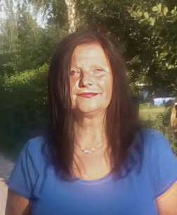Portr&auml;t einer Frau mit langen, dunklen Haaren und blauem Shirt, vor einer gr&uuml;nen, bewaldeten Kulisse.