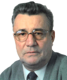 Portr&auml;t eines &auml;lteren Mannes mit Brille, grauem Haar und einem grauen Pullover, vor hellem Hintergrund.