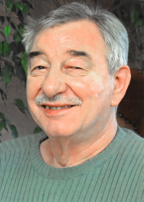 L&auml;chelnder &auml;lterer Mann mit grauen Haaren, der einen gr&uuml;nen Pullover tr&auml;gt, vor einer unauff&auml;lligen Hintergrundumgebung.