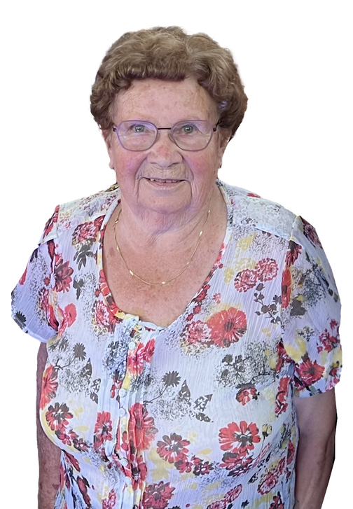 Portr&auml;t einer &auml;lteren Frau mit kurzem, lockigem Haar und bl&uuml;hendem, farbenfrohem Shirt, l&auml;chelnd vor wei&szlig;em Hintergrund.