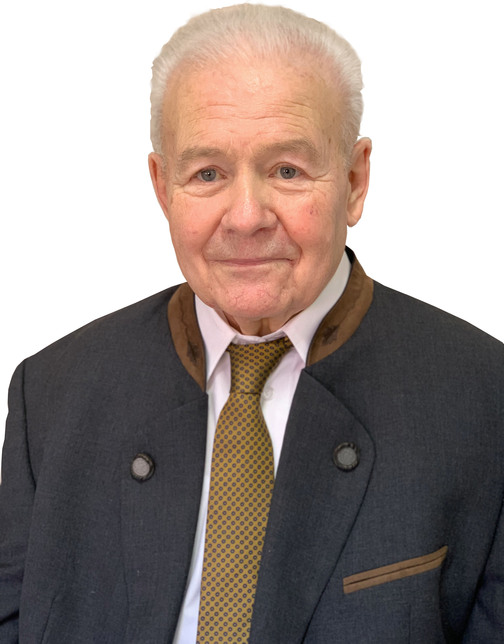 Portr&auml;t eines &auml;lteren Mannes mit grauen Haaren, Anzugjacke und gebl&uuml;mtem Krawatte vor neutralem Hintergrund.