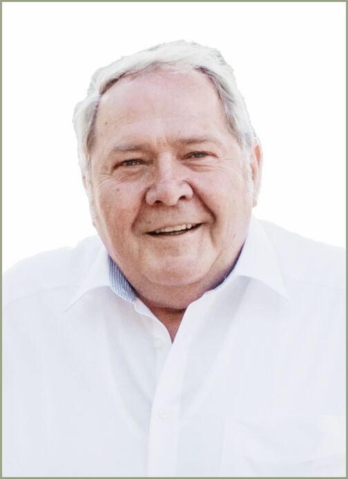 L&auml;chelnder &auml;lterer Mann mit kurzem grauem Haar, getragenem wei&szlig;en Hemd, vor hellem Hintergrund.