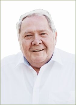 L&auml;chelnder &auml;lterer Mann mit kurzem grauem Haar, getragenem wei&szlig;en Hemd, vor hellem Hintergrund.