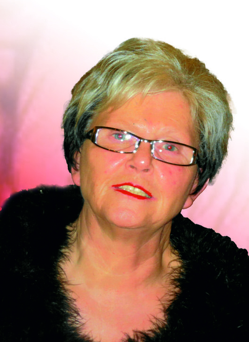 Portr&auml;t einer &auml;lteren Frau mit Brille, grauen Haaren und rotem Lippenstift, vor einem sanften rosa Hintergrund.