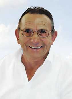 L&auml;chelnder &auml;lterer Mann mit Brille und wei&szlig;em Hemd vor einem hellblauen, wolkigen Hintergrund.