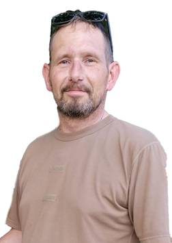 Mann mit kurzem Haar und Brille, tr&auml;gt ein beige T-Shirt und l&auml;chelt vor einem wei&szlig;en Hintergrund.