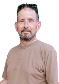 Mann mit kurzem Haar und Brille, tr&auml;gt ein beige T-Shirt und l&auml;chelt vor einem wei&szlig;en Hintergrund.