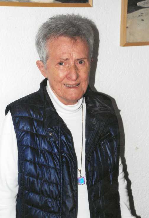 Portr&auml;t einer &auml;lteren Person mit kurzem grauem Haar, tragt eine dunkelblaue Weste und ein wei&szlig;es Oberteil, vor einer hellen Wand.