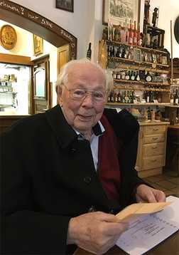&Auml;lterer Mann im Caf&eacute;, der auf einem Men&uuml;blatt schaut und einen Briefumschlag in der Hand h&auml;lt, umgeben von Holzregalen.