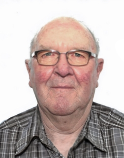 Porträt eines älteren Mannes mit Brille und kariertem Hemd vor einfarbigem Hintergrund.