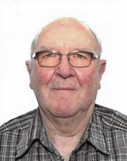 Portr&auml;t eines &auml;lteren Mannes mit Brille und kariertem Hemd vor einfarbigem Hintergrund.