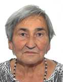 Portr&auml;t einer &auml;lteren Frau mit grauen Haaren und einem bunten Oberteil, vor hellem Hintergrund. Sie tr&auml;gt eine Halskette.