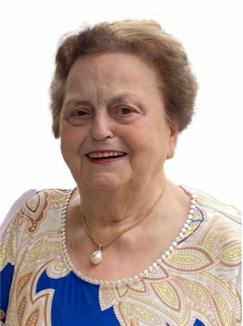 L&auml;chelnde &auml;ltere Frau mit kurzem braunem Haar, tragt ein buntes, gemustertes Oberteil und eine Perlenkette.