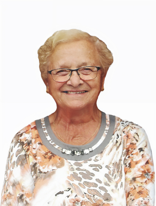 L&auml;chelnde &auml;ltere Frau mit Brille, tr&auml;gt ein buntes Oberteil, vor einem wei&szlig;en Hintergrund.