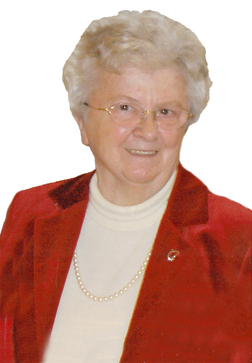 &Auml;ltere Frau mit grauen Haaren, Brille, rotem Blazer und Perlenkette, l&auml;chelt vor einem wei&szlig;en Hintergrund.