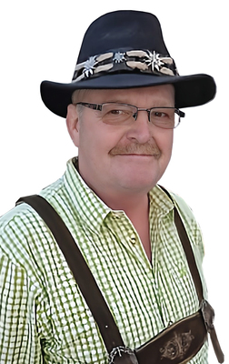 Mann mit Brille, Holzf&auml;llerhemd und schwarzem Hut, l&auml;chelt in die Kamera vor einem wei&szlig;en Hintergrund.