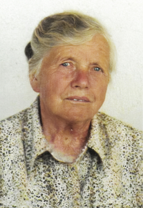 Portr&auml;t einer &auml;lteren Frau mit blonden Haaren, die ein gemustertes Hemd tr&auml;gt, vor einer hellen Hintergrundfl&auml;che.