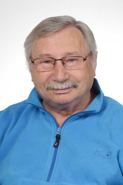 Portr&auml;t eines &auml;lteren Mannes mit Brille, grauen Haaren und Schnurrbart, der einen blauen Fleece-Pullover tr&auml;gt.