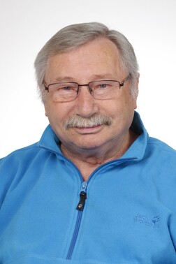 Portr&auml;t eines &auml;lteren Mannes mit Brille, grauen Haaren und Schnurrbart, der einen blauen Fleece-Pullover tr&auml;gt.