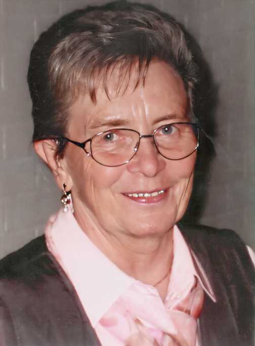 L&auml;chelnde Frau mit Brille, kurzem Haar und Ohrringen, in rosa Bluse und Weste vor neutralem Hintergrund.