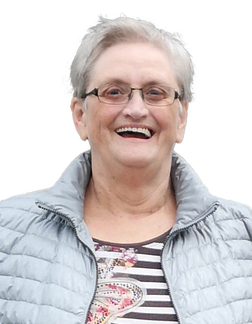 L&auml;chelnde &auml;ltere Frau mit Brille, tr&auml;gt eine graue Jacke &uuml;ber einem gestreiften Oberteil.