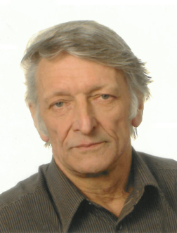 Portr&auml;t eines &auml;lteren Mannes mit grauen Haaren, der einen braunen Hemd tr&auml;gt, vor einem hellen Hintergrund.