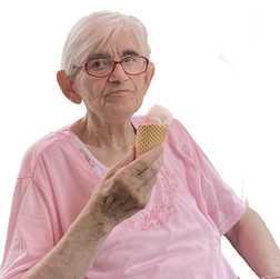 &Auml;ltere Frau mit Brille h&auml;lt ein Waffeleis mit rosa Eis und schaut neutral in die Kamera, tr&auml;gt ein pinkes Oberteil.