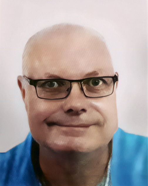 Nahaufnahme eines l&auml;chelnden Mannes mit Brille, kurzem, lichtem Haar und blauem Oberteil vor einem hellen Hintergrund.