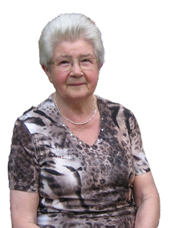 &Auml;ltere Frau mit Brille und hellerem Haar in leopardenmuster-Shirt, sitzt mit leicht l&auml;chelndem Gesicht vor einem wei&szlig;en Hintergrund.