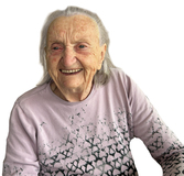 Lächelnde ältere Frau mit langen grauen Haaren, trägt einen hellrosa Pullover mit schwarzem Muster.