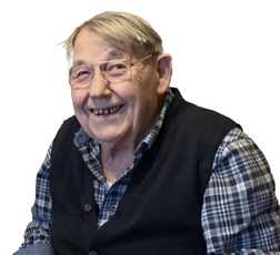 L&auml;chelnder &auml;lterer Mann mit Brille, in einer karierter Bluse und Weste, posiert vor einem wei&szlig;en Hintergrund.