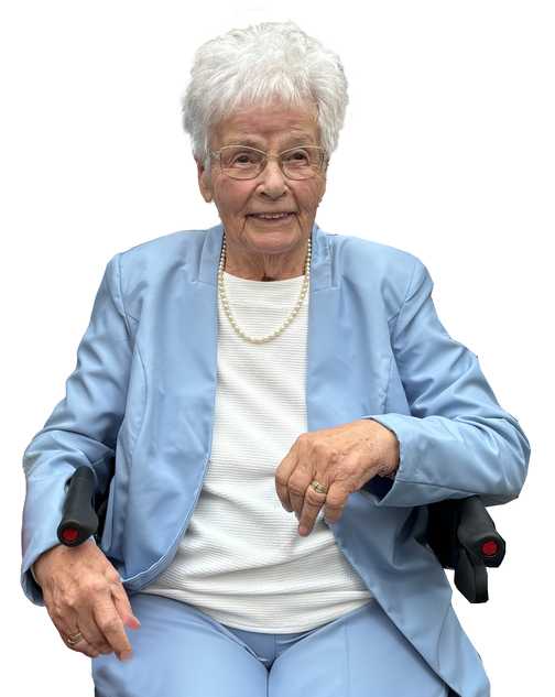 &Auml;ltere Frau mit wei&szlig;en Haaren, Brille und Perlenschmuck, tr&auml;gt einen blauen Anzug und sitzt auf einem Rollstuhl.