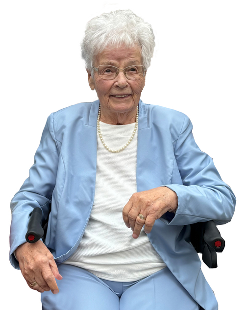 &Auml;ltere Frau mit wei&szlig;en Haaren, Brille und Perlenschmuck, tr&auml;gt einen blauen Anzug und sitzt auf einem Rollstuhl.