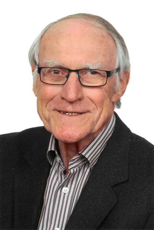 Portrait eines &auml;lteren Mannes mit Brille, grauen Haaren und einem freundlichen L&auml;cheln, in einem gestreiften Hemd und Jackett.