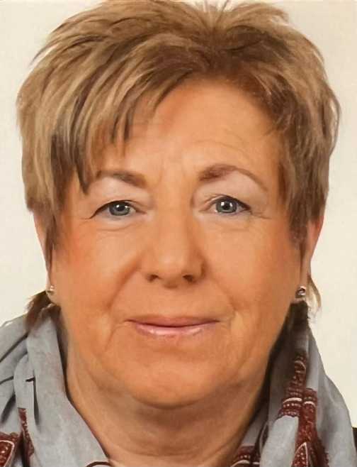 Bildausschnitt eines l&auml;chelnden, mittelalten Frauengesichts mit kurzen, blonden Haaren und einem grauen Schal.