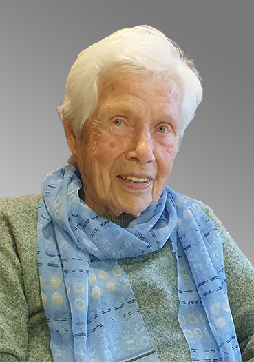 Portr&auml;t einer &auml;lteren Person mit grauem Haar, die einen blauen Schal tr&auml;gt und in die Kamera l&auml;chelt.